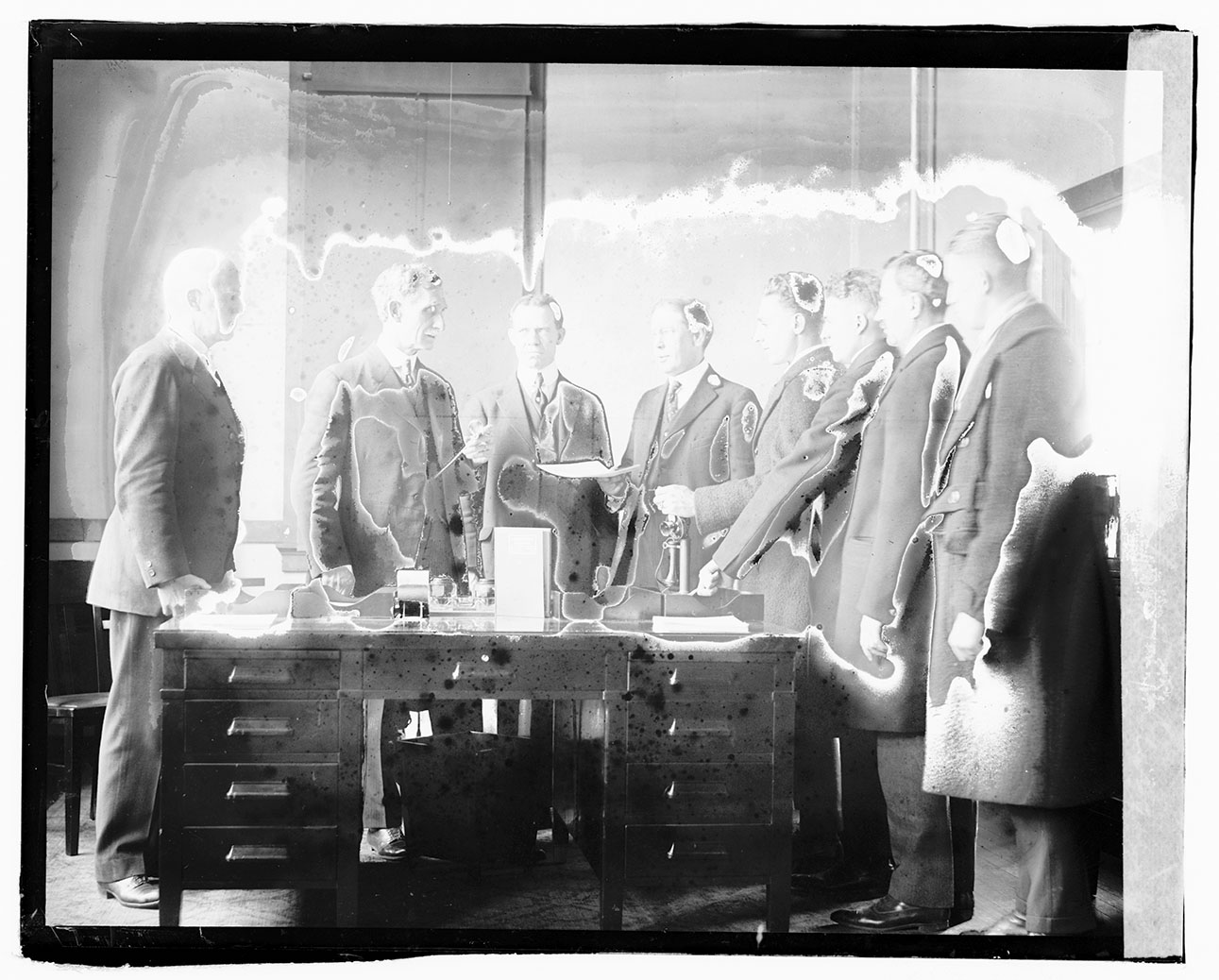 men standing around a wooden desk, Steuart to the far left