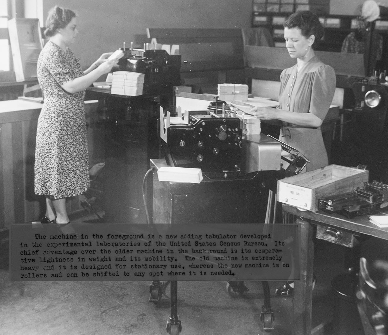 "The machine in the foreground is a new adding tabulator" featuring two women workers and two machines in what appears to be the mechanical lab